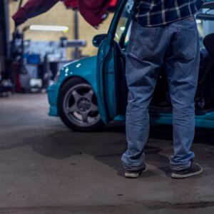 man in blue denim jeans and black leather boots standing beside blue car during daytime