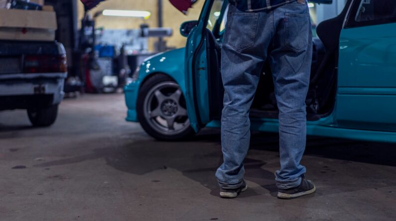 man in blue denim jeans and black leather boots standing beside blue car during daytime